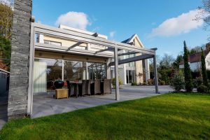 An awning overhanging a pergola in a residential garden with a table and chairs underneath